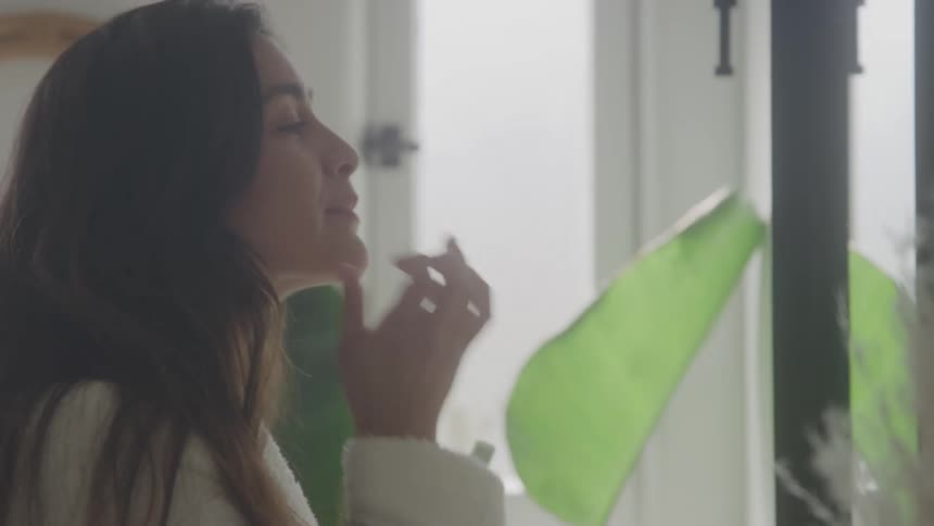 The woman is putting on lipstick in the mirror
