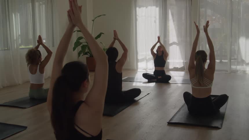 A group of women sitting crosslegged on yoga mats in a room on a yoga studio setting