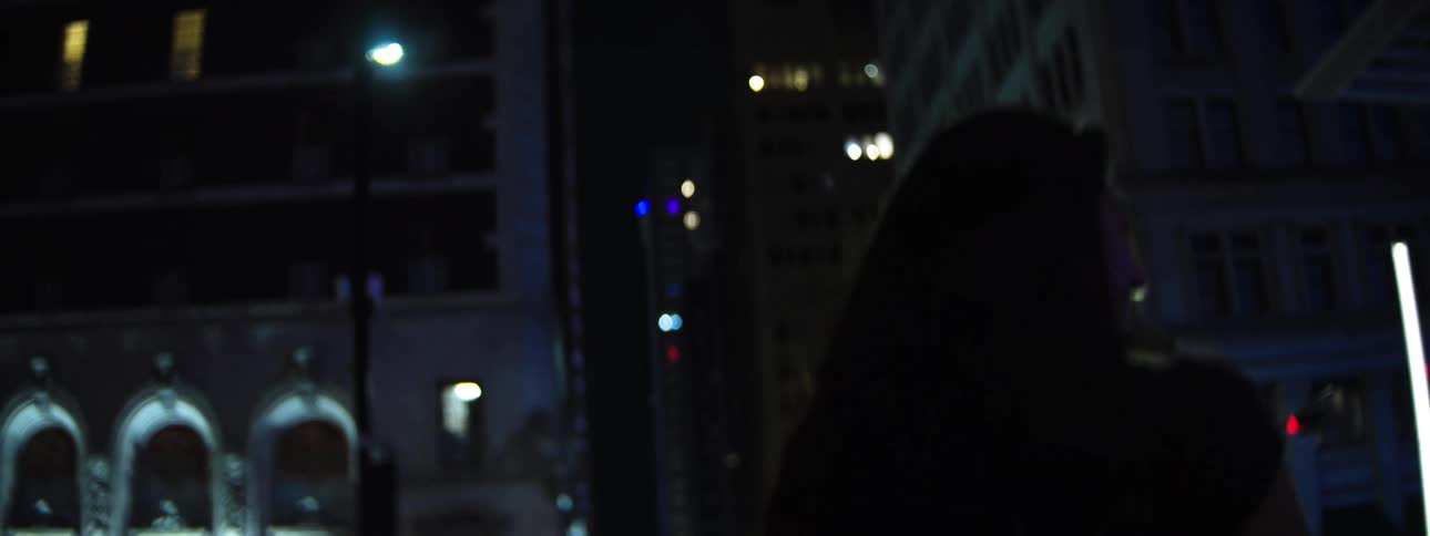 Female pedestrian walking through downtown at night approaches an intersection