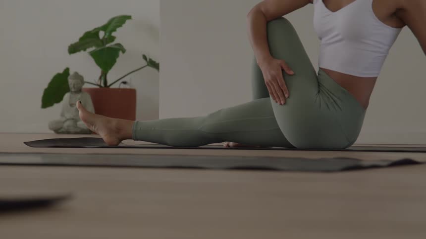 A woman sits on a floor mat and does a yoga pose
