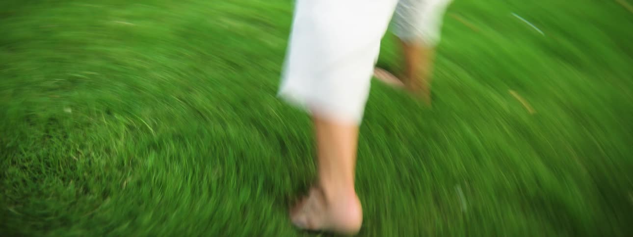 Bare feet walk on green grass in motion