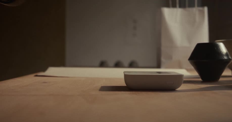 A hand brings a smart phone to a device on a table they touch for a second then the hand pulls the phone away again