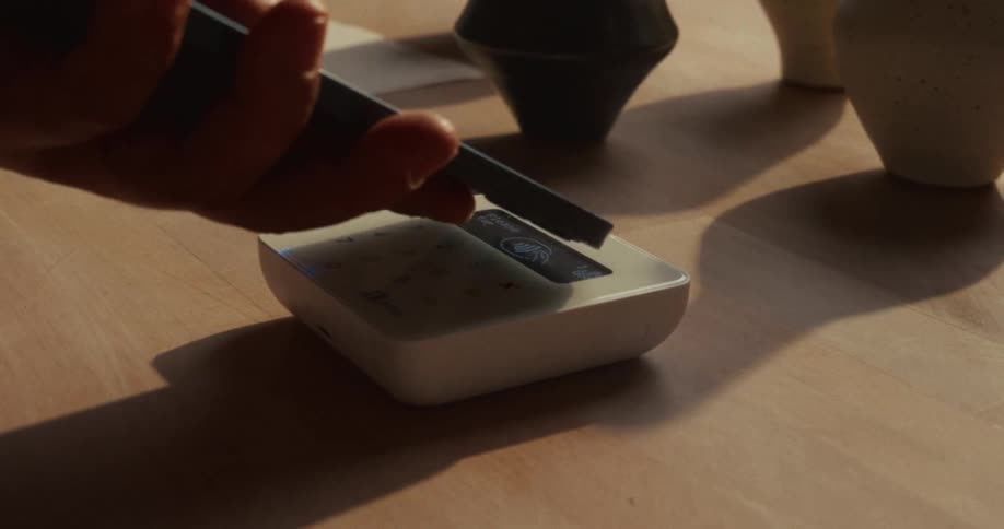 Close up of a person making a payment with their phone through a payment machine placed on a tabletop
