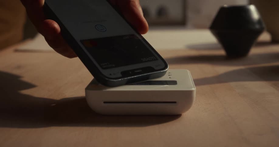Hand bringing a smartphone close to a card reader for contactless payment