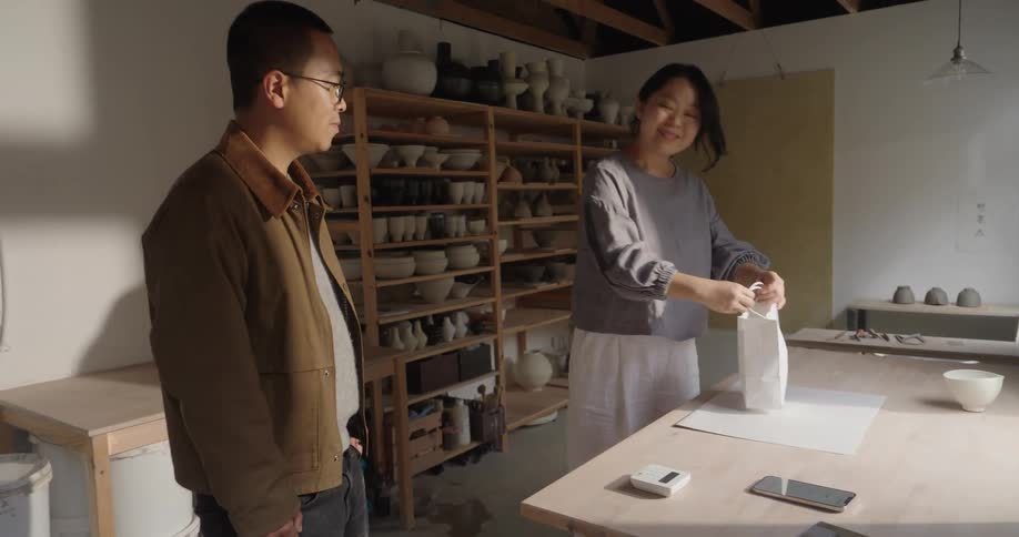 Man receives a bag from a woman in a store with shelves full of objects in the background
