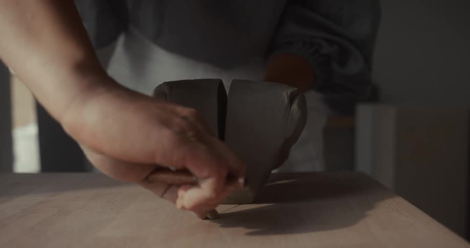 Female potter uses a tool with a wire to slice a piece of clay in half
