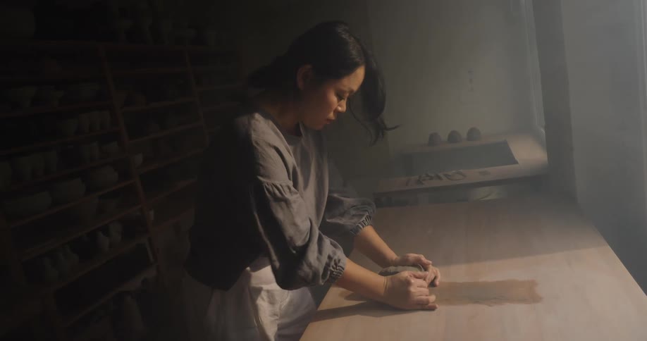 Woman shapes clay on a table in a pottery studio setting