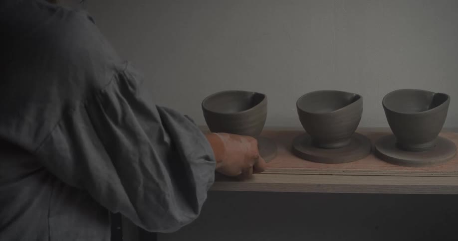 Person arranges freshly shaped ceramic pieces on a shelf