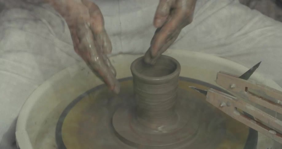 Hands shaping a clay piece on a pottery wheel