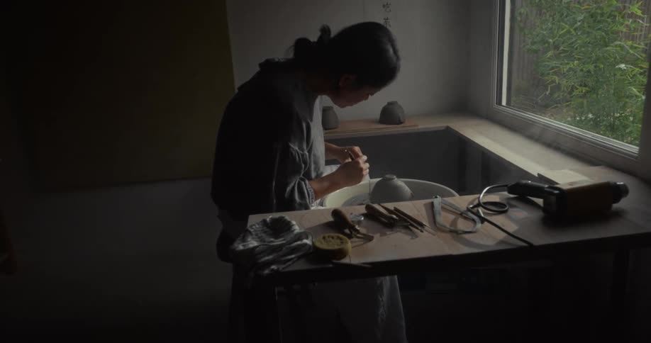 Woman works on a pottery wheel using tools in a studio