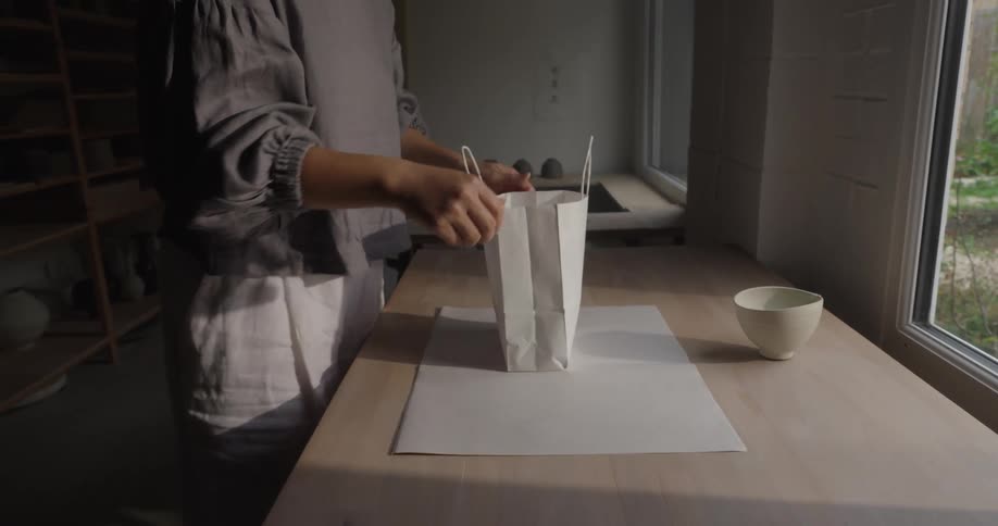 A young asian woman packaging an order bag for a ceramic bowl in a pottery room during daytime