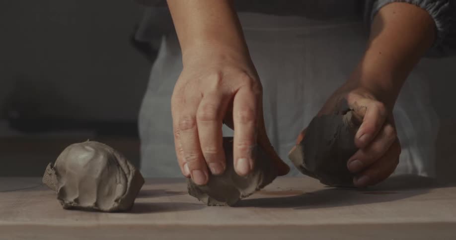 Close up of a woman dividing kneaded clay on a wooden tabletop in a room during daytime