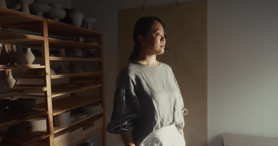 Woman standing indoors next to shelves with ceramics