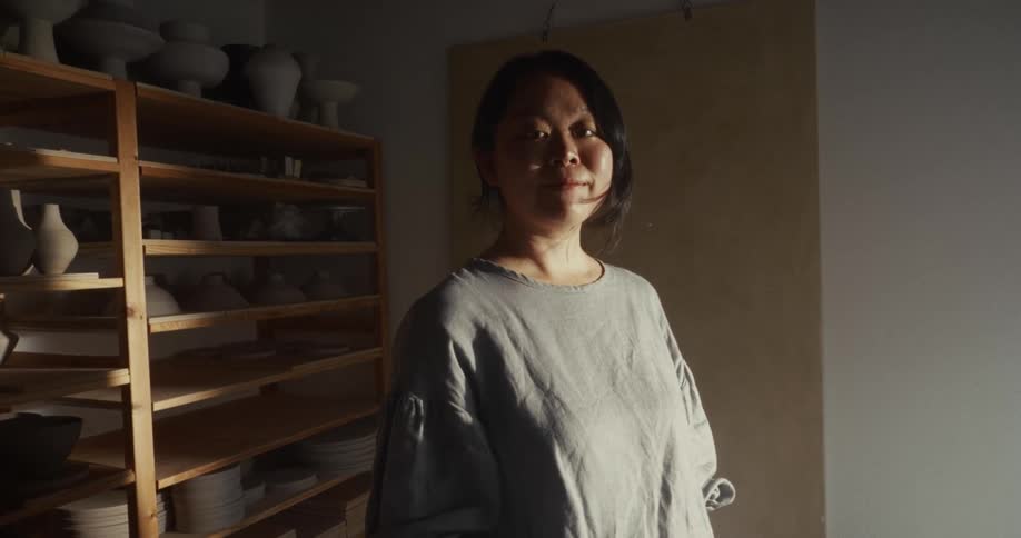 An asian woman standing in a room with shelves of ceramic objects