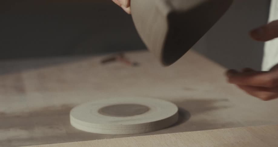Potter picks a clay bowl from thedisk it was drying on and places it upside down on a wood surface