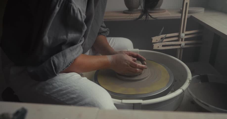Woman shapes clay on a pottery wheel inside a studio