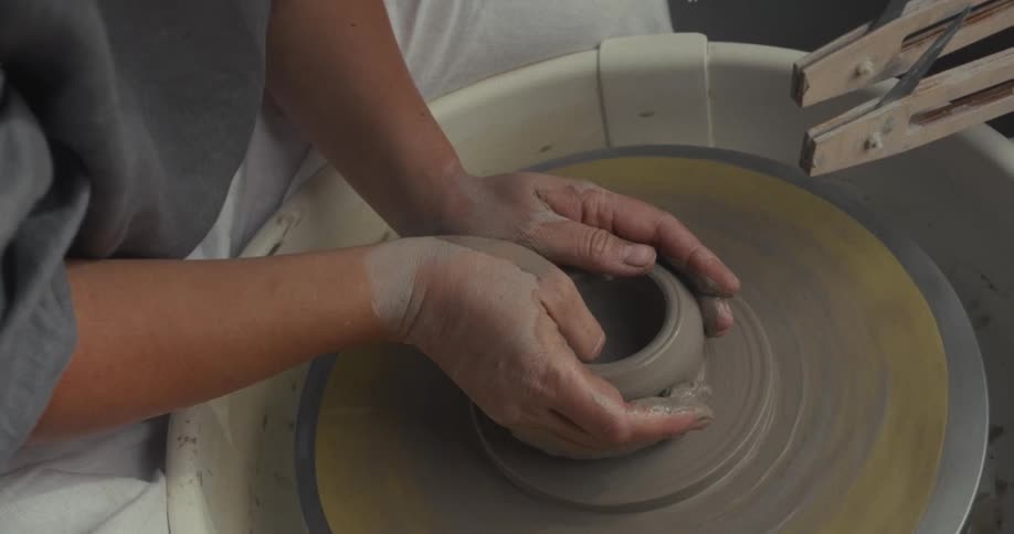 Hands shaping a wet ceramic piece on a pottery wheel