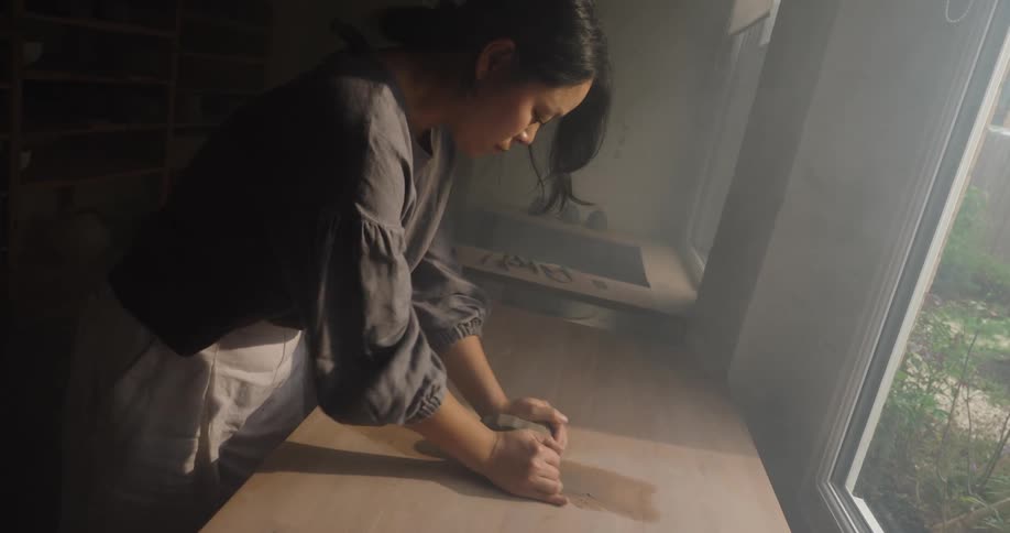 Person kneading clay near a window lit by natural light