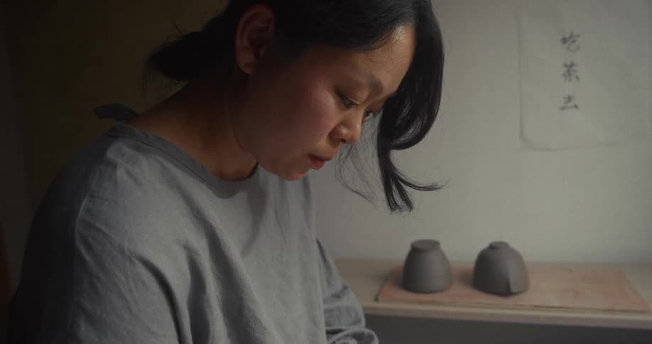 Person works with ceramics in a studio with clay pieces drying on a shelf in the background