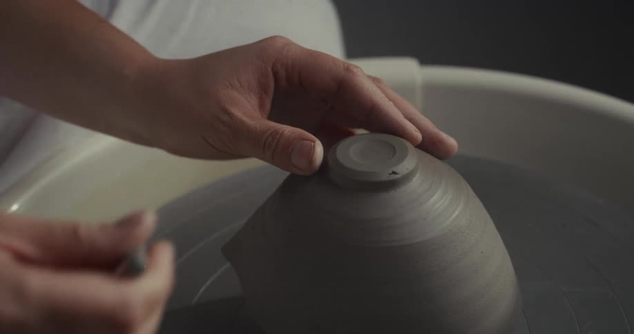 Close up of a woman finishing a clay bowl with a tool on a pottery wheel