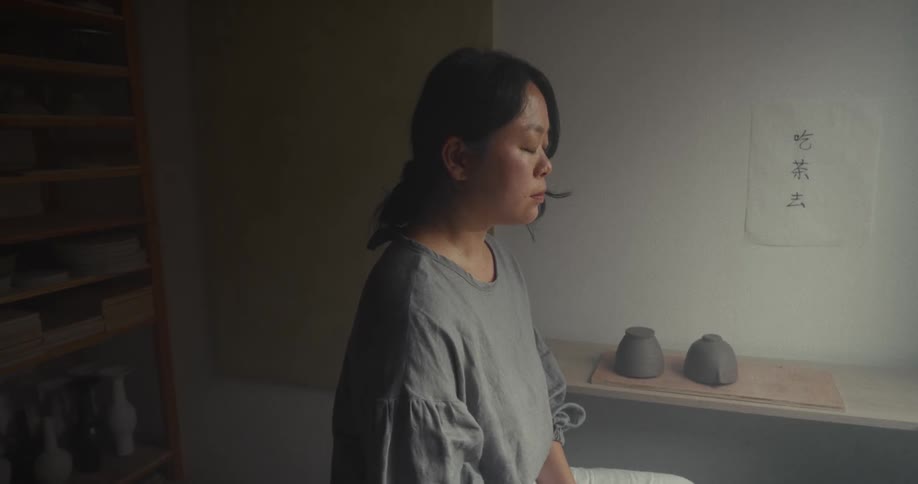 Close up of a young asian woman meditating while sitting in front of a pottery wheel on a room during daytime
