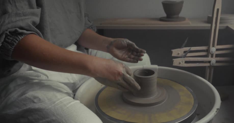 The woman makes a cup on the pottery wheel