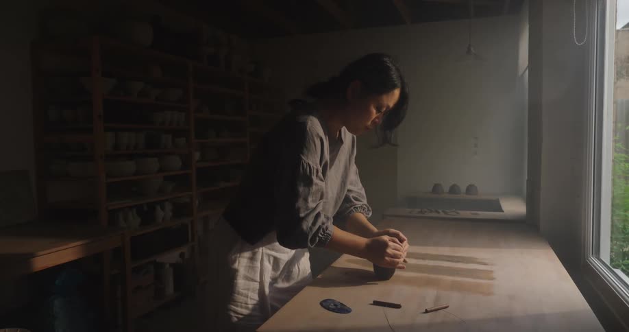 A young asian woman kneading clay on a table surface for pottery in a pottery room during daytime