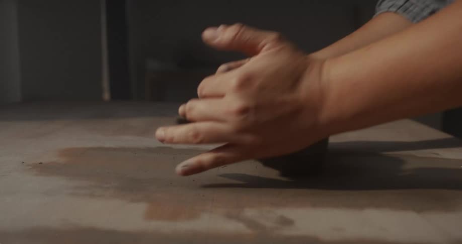 Hands turning and shaping a lump of clay on the table