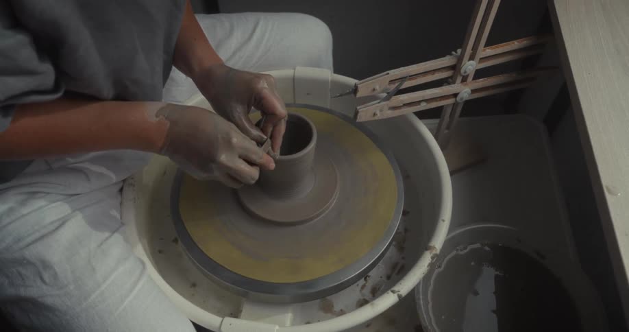 A person works at a rotating pottery wheel at midday shaping a vase from clay