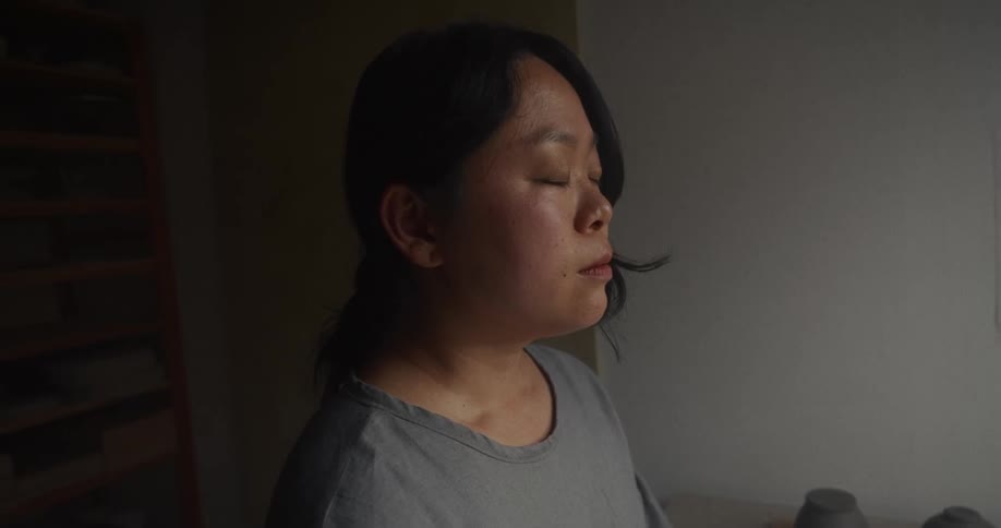 Close up portrait of a young asian woman meditating while sitting in a pottery room during daytime