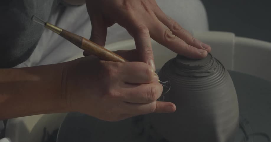 Close up of a woman using a tool to remove excess clay from a pottery bowl on a pottery wheel