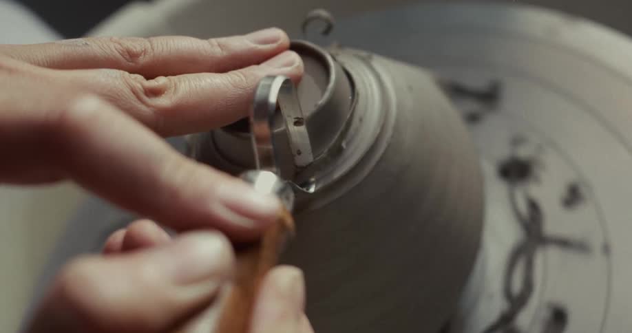 Potter uses a tool to shave clay off an object turning on a pottery wheel