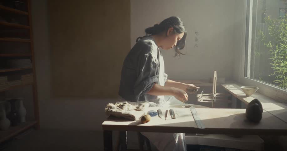 Woman shaping pottery on a wheel beside work tools