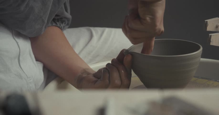 Hands carve the details of a ceramic vase on a pottery wheel