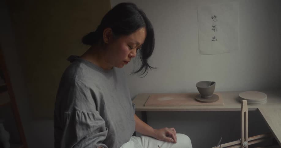 Female potter shapes the piece of clay turning on a pottery wheel while in her workshop