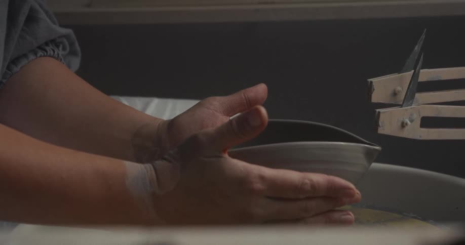 Hands holding a shaped ceramic bowl on the wheel