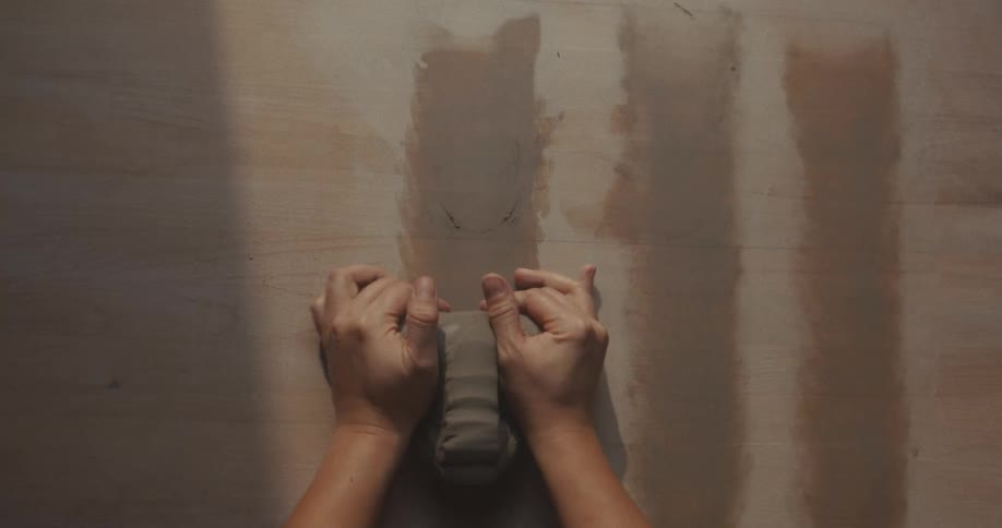 Hands preparing clay on a wooden surface