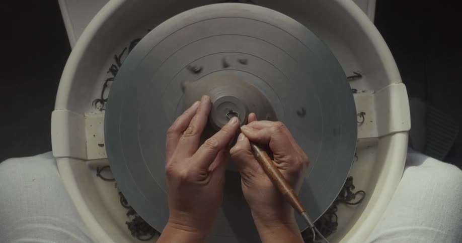 A young woman using a tool to finish a clay pottery on a rotating pottery wheel