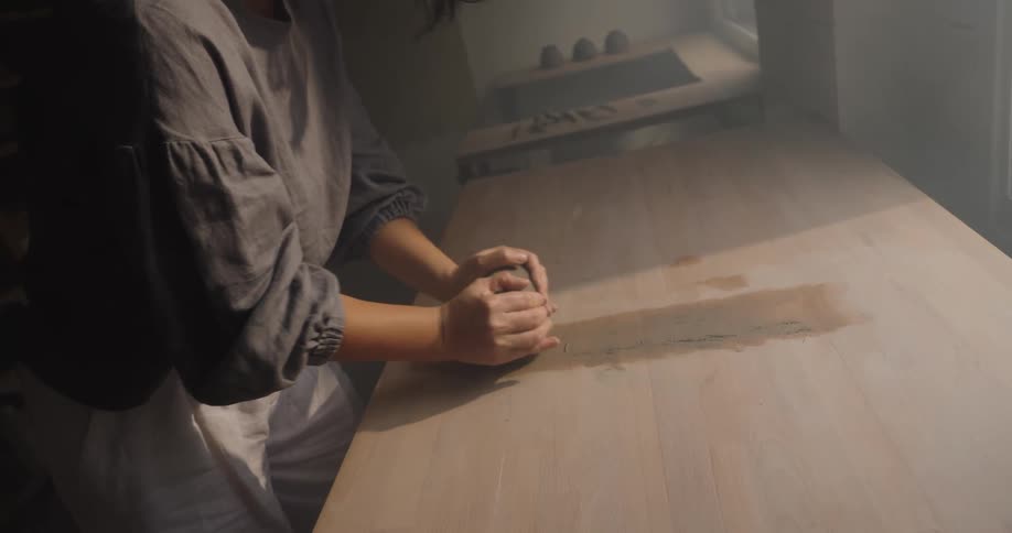 Close up of a young asian woman kneading clay on a table surface in a pottery room during daytime