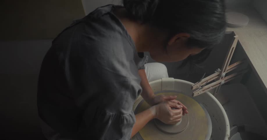 A young asian woman moulding pottery on a pottery wheel in a room during daytime