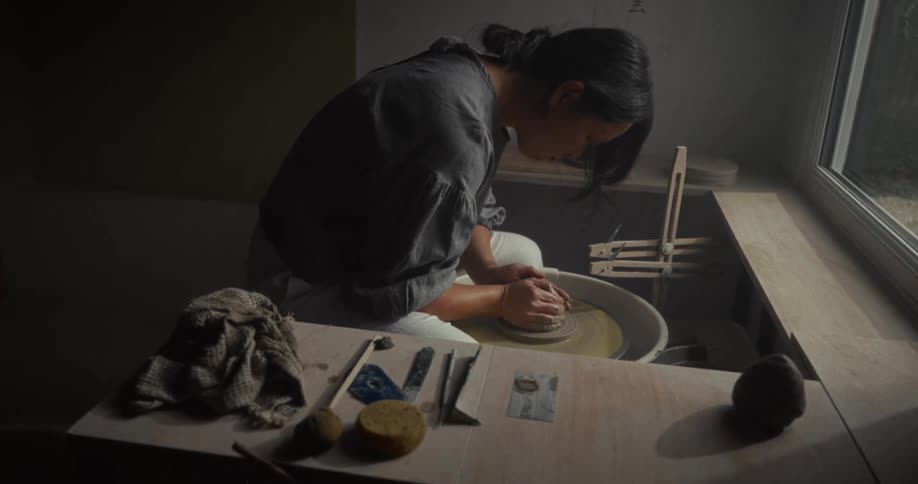 Woman shaping clay on a pottery wheel inside a sunlit studio