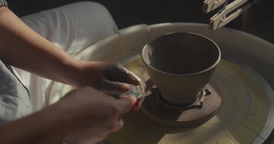 Hands position a ceramic vase on the pottery wheel during the shaping process