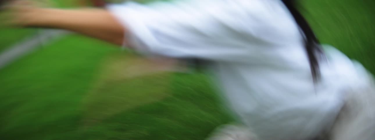 A young hispanic woman wearing a light shirt and light pants moves their body vigorously on a patch of green ground