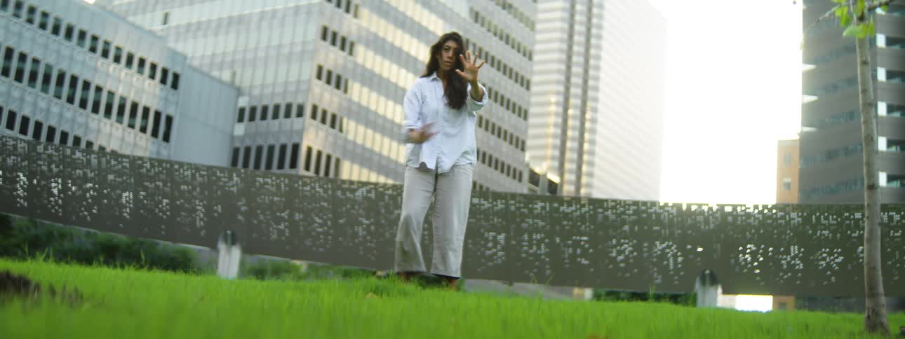 Woman dancing barefoot in a green space surrounded by buildings