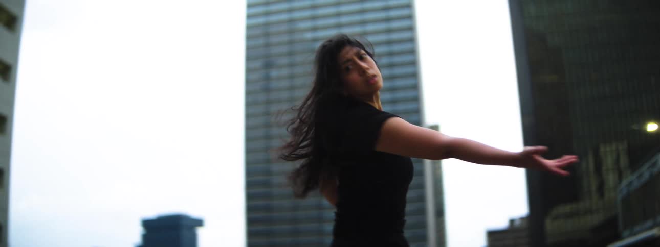 Woman dancing with expressive movements among tall buildings