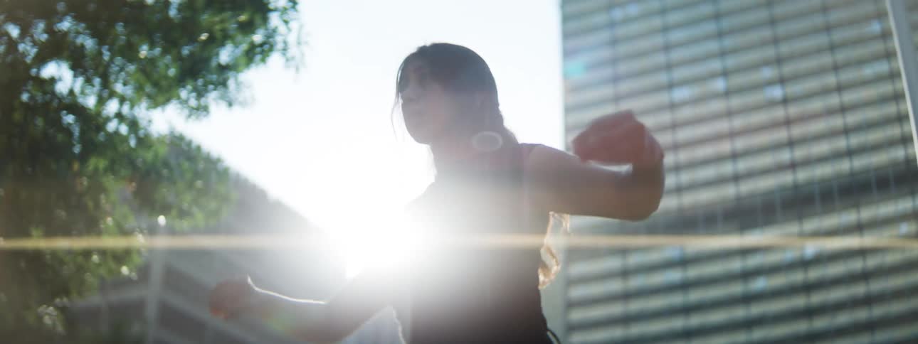 Woman dancing under sunlight among urban buildings