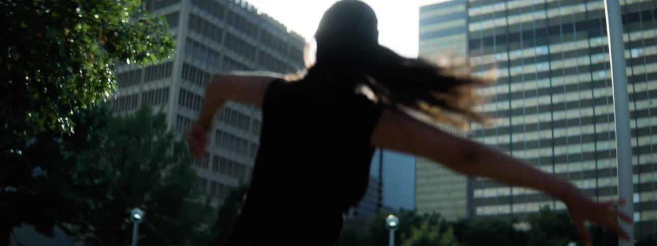 The silhouette of a hispanic woman with long hair moving and stretching their body in a street setting