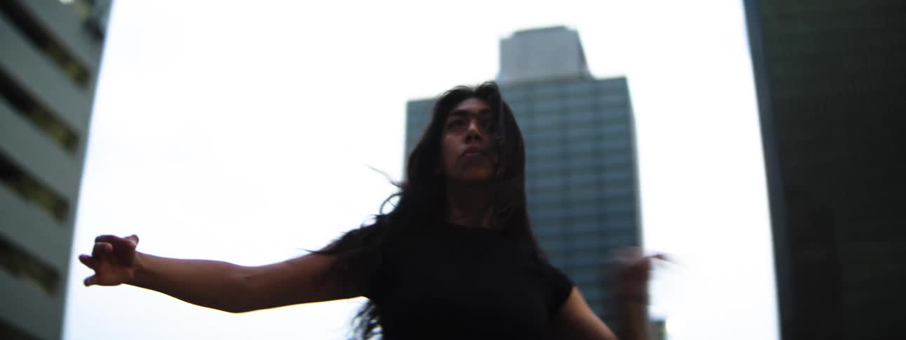 A hispanic woman with long dark hair wearing dark clothes moving their arms and body in an expressive manner