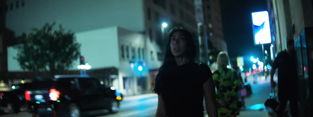 Woman walks along a brightly lit street at night in an urban setting