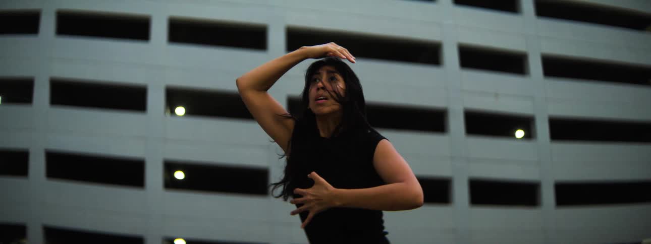Woman dances outdoors with expressive movements in front of a building